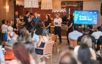 À direita, uma tela de TV exibe a identidade visual do evento com o título 