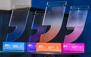 Esta imagem exibe troféus da etapa regional de Minas Gerais do Prêmio Sebrae de Jornalismo, organizados em linha sobre uma superfície de vidro.