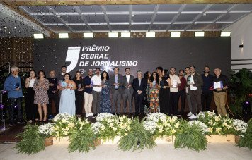 Esta imagem registra a foto oficial coletiva dos premiados e organizadores ao final da cerimônia da 13ª Edição do Prêmio Sebrae de Jornalismo. Um grande grupo com cerca de 20 pessoas (jornalistas finalistas, vencedores e executivos do Sebrae) posa alinhado e sorridente no palco.
