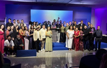 Esta imagem registra a fotografia coletiva oficial dos vencedores, finalistas e comissão organizadora ao encerramento de uma cerimônia do Prêmio Sebrae de Jornalismo. Uma ampla equipe de jornalistas e executivos do Sebrae posa sorridente, distribuídos entre o plano frontal e os degraus do palco central. Diversos premiados seguram seus troféus em acrílico com as bases coloridas representativas das diferentes modalidades do prêmio.